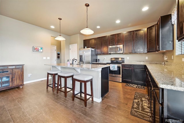 12766 Sunlight Peak Pl, Peyton, CO 80831 - kitchen with stainless steel appliances, recessed lighting, a kitchen island with sink, a breakfast bar, and dark brown cabinetry