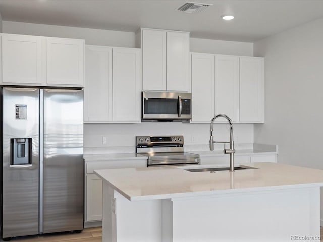 kitchen featuring visible vents, white cabinets, an island with sink, stainless steel appliances, and a sink