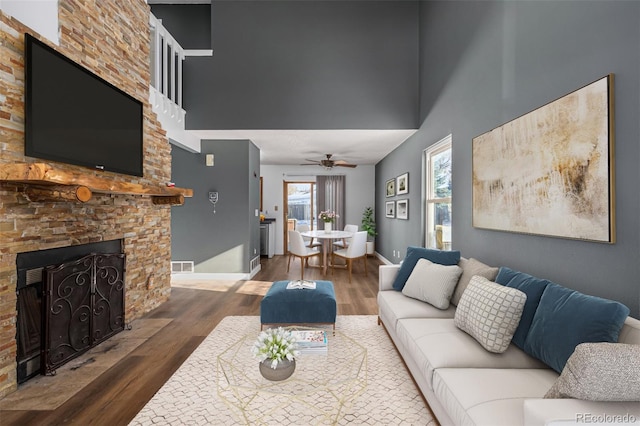 living room with a fireplace, hardwood / wood-style floors, ceiling fan, and a high ceiling