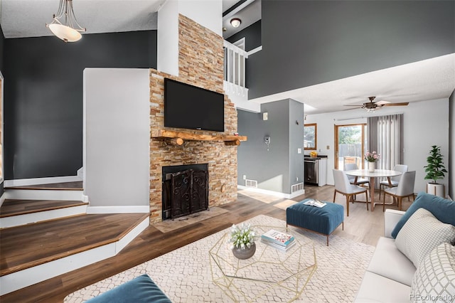 living room featuring a textured ceiling, vaulted ceiling, ceiling fan, hardwood / wood-style floors, and a stone fireplace