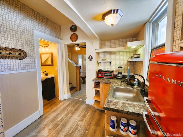 kitchen featuring light wood finished floors, wallpapered walls, open shelves, a sink, and dark countertops