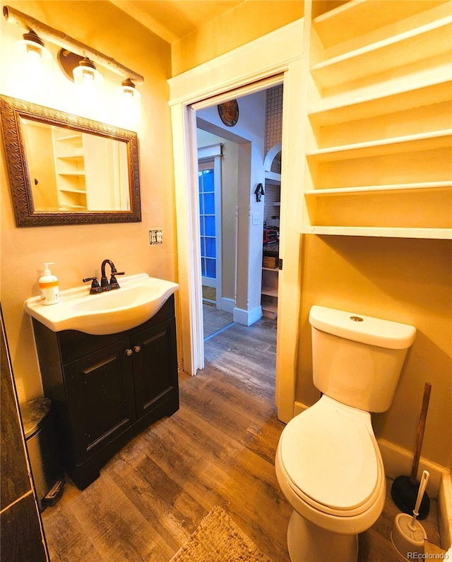 half bathroom featuring vanity, toilet, wood finished floors, and baseboards