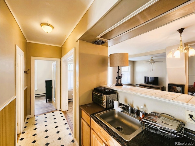 kitchen with light floors, ceiling fan, a sink, crown molding, and baseboard heating