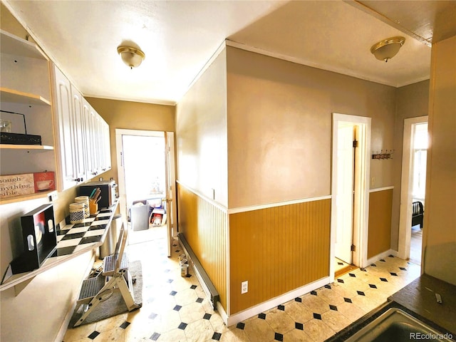 hall featuring wainscoting, wood walls, light floors, and ornamental molding