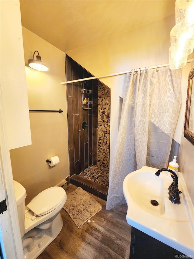 bathroom with tiled shower, toilet, wood finished floors, and vanity