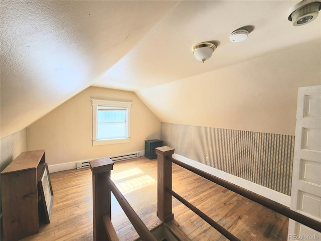 additional living space featuring vaulted ceiling, a baseboard radiator, baseboards, and hardwood / wood-style flooring