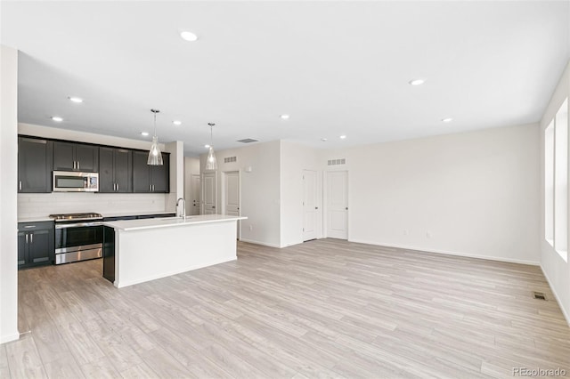 13342 E 110th Way, Commerce City, CO 80022 - kitchen with appliances with stainless steel finishes, backsplash, recessed lighting, an island with sink, and light wood-style floors