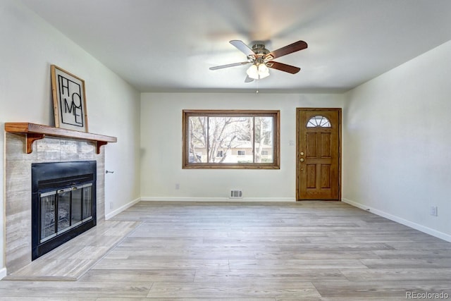 unfurnished living room with a ceiling fan, a fireplace, visible vents, and light wood-type flooring