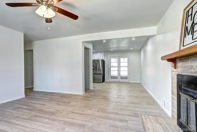 unfurnished living room with a tiled fireplace, a ceiling fan, light wood-style floors, and baseboards