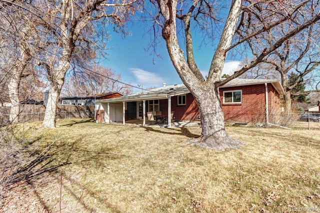 rear view of property with brick siding, a lawn, a patio, and fence