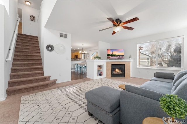 living room featuring ceiling fan with notable chandelier, light colored carpet, and a tiled fireplace