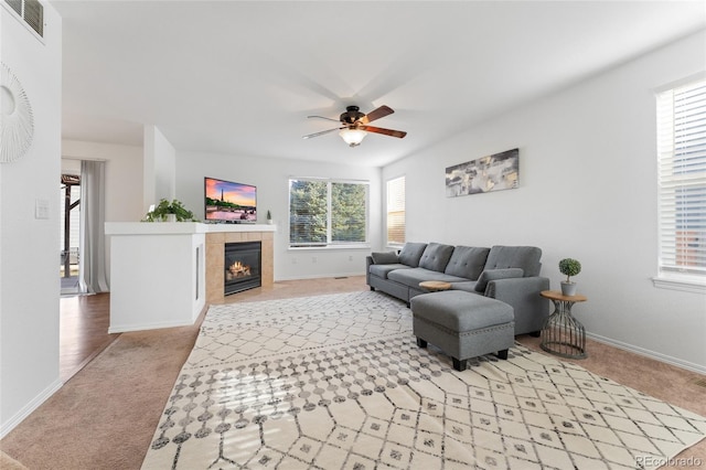 living room with a tiled fireplace, ceiling fan, and light colored carpet