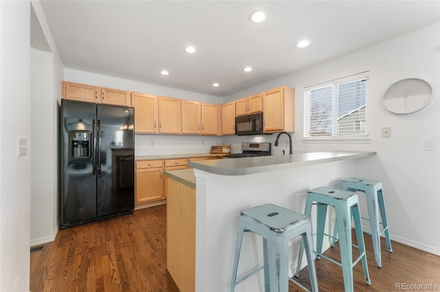 kitchen with kitchen peninsula, a breakfast bar, black appliances, light brown cabinets, and dark hardwood / wood-style floors