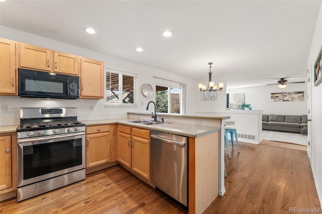 kitchen with ceiling fan with notable chandelier, sink, light hardwood / wood-style floors, kitchen peninsula, and stainless steel appliances