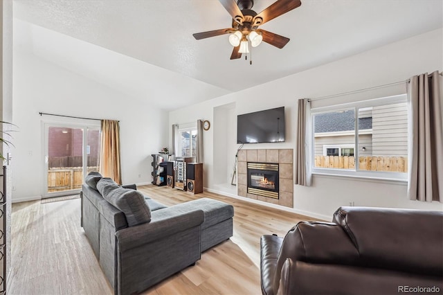 living room featuring lofted ceiling, wood finished floors, baseboards, ceiling fan, and a tile fireplace