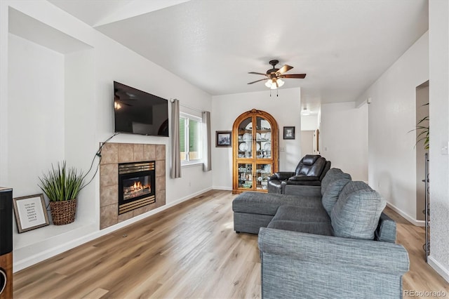 living area featuring a fireplace, baseboards, light wood finished floors, and ceiling fan