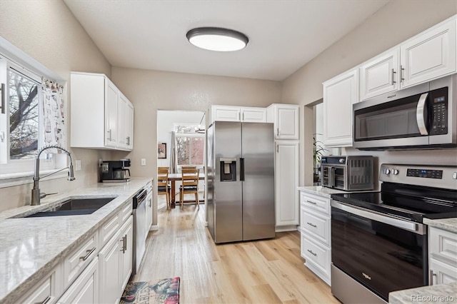 kitchen with light stone counters, appliances with stainless steel finishes, light wood-style floors, and a sink