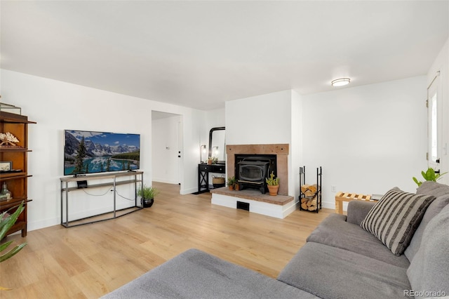 living room featuring light wood-type flooring, a tile fireplace, and a wood stove