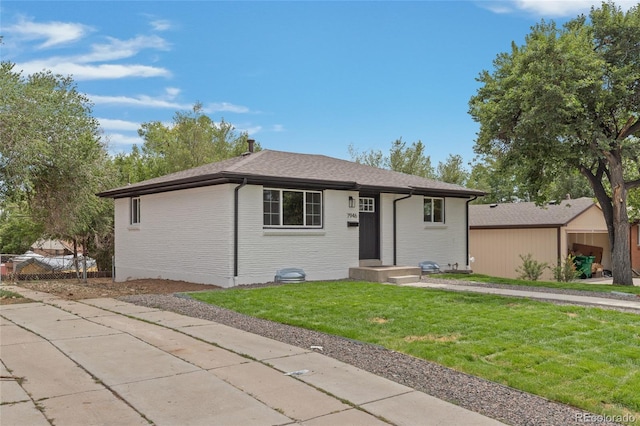 ranch-style house with roof with shingles, a front yard, fence, and brick siding