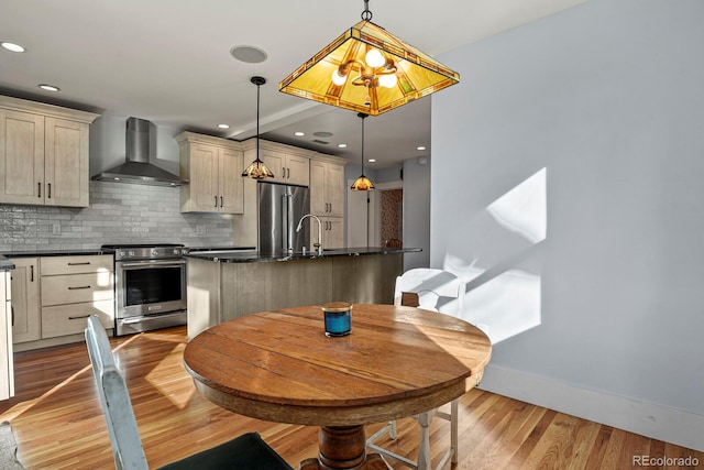 kitchen featuring wall chimney range hood, stainless steel appliances, pendant lighting, light wood-type flooring, and tasteful backsplash