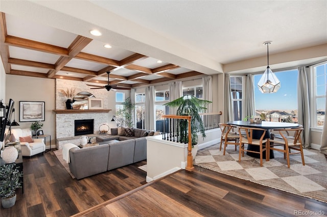 living room with dark wood-type flooring, coffered ceiling, a stone fireplace, beamed ceiling, and ceiling fan