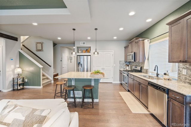 kitchen with light wood-type flooring, a center island, hanging light fixtures, backsplash, and appliances with stainless steel finishes