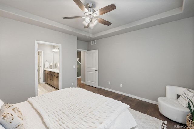 bedroom with a tray ceiling, dark wood-type flooring, ceiling fan, and ensuite bathroom