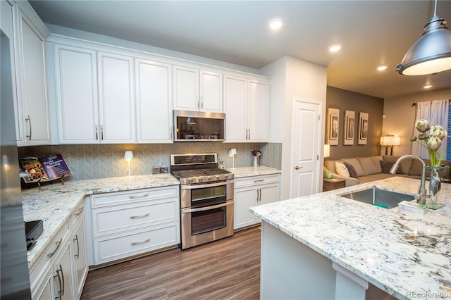 359 Courtfield Way, Castle Pines, CO 80108 - kitchen with appliances with stainless steel finishes, a sink, wood finished floors, open floor plan, and backsplash