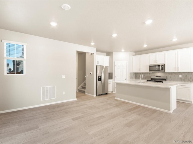 kitchen with white cabinetry, tasteful backsplash, a kitchen island with sink, stainless steel appliances, and light hardwood / wood-style floors