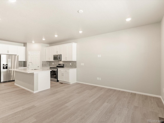 kitchen with sink, appliances with stainless steel finishes, white cabinetry, backsplash, and an island with sink