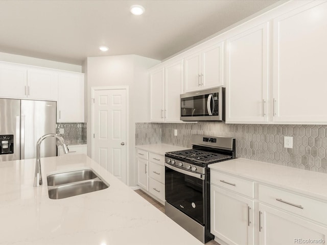 kitchen with appliances with stainless steel finishes, white cabinetry, sink, backsplash, and light stone counters