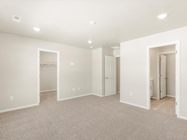 unfurnished bedroom featuring a spacious closet, light carpet, and a closet