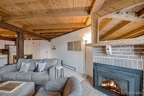 8500 Ryan Gulch Rd Unit 101, Silverthorne, CO 80498 - living room featuring wood ceiling, beamed ceiling, a lit fireplace, and a baseboard radiator