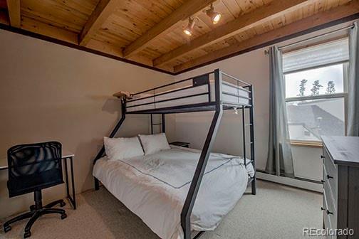 8500 Ryan Gulch Rd Unit 101, Silverthorne, CO 80498 - bedroom with wooden ceiling, baseboard heating, multiple windows, light carpet, and beam ceiling
