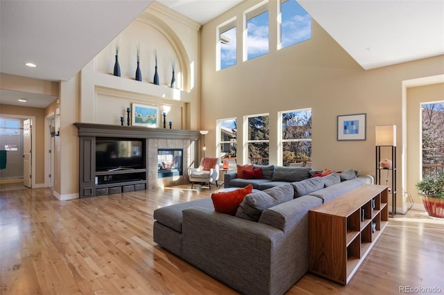 living room featuring a tile fireplace, light wood-type flooring, and a towering ceiling