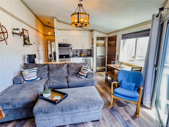 living room with lofted ceiling, an inviting chandelier, crown molding, and wood finished floors