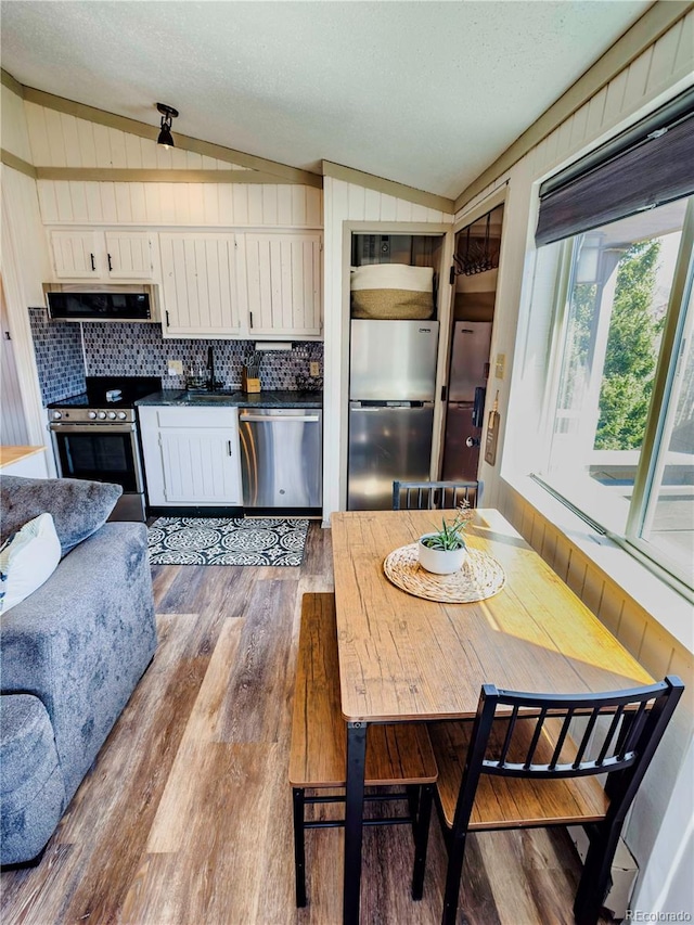 kitchen with vaulted ceiling, dark countertops, white cabinets, appliances with stainless steel finishes, and wood finished floors
