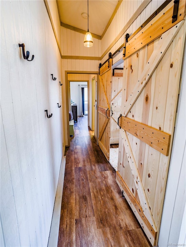 hallway with dark wood-type flooring, wooden walls, and a barn door
