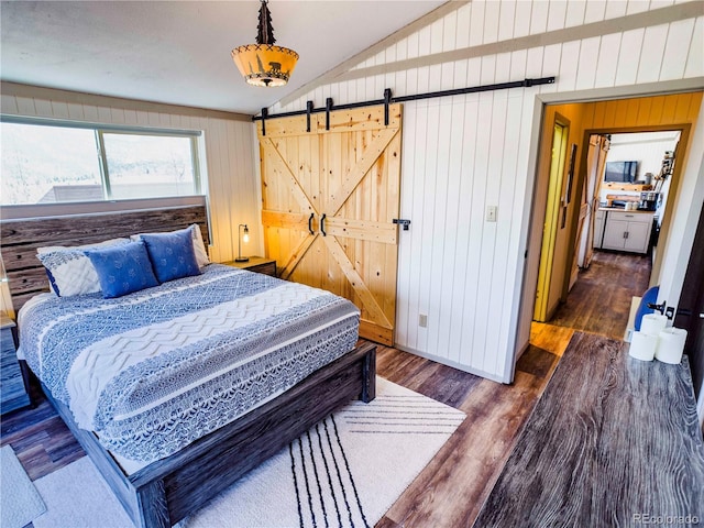 bedroom with lofted ceiling, a barn door, wooden walls, and dark wood finished floors