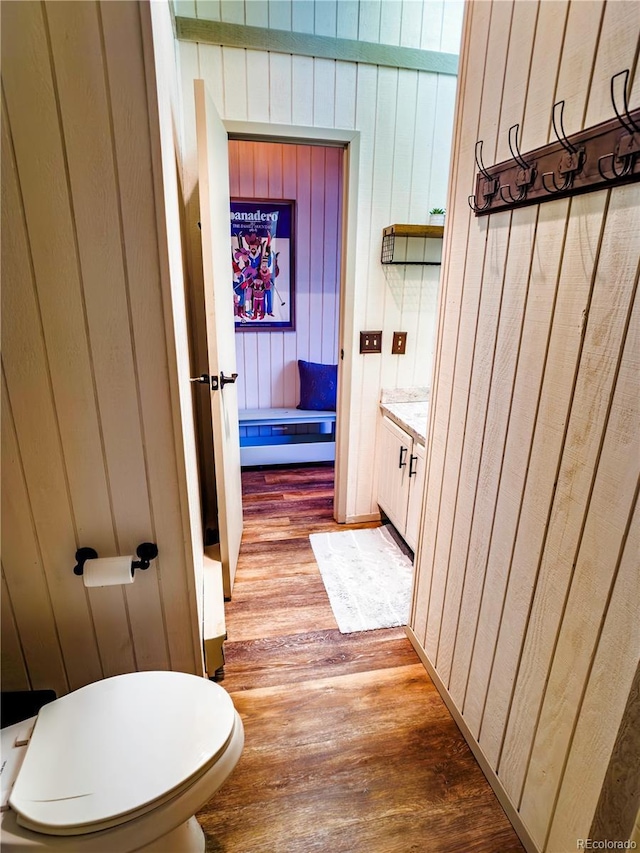half bath with wooden walls, toilet, vanity, and wood finished floors