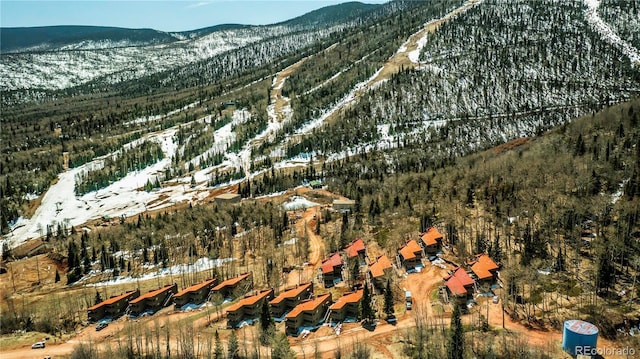 snowy aerial view featuring a wooded view and a mountain view