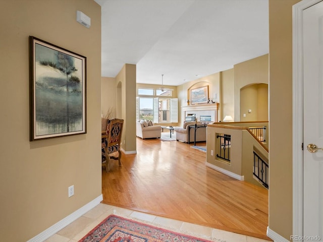 hallway with arched walkways, baseboards, and tile patterned flooring