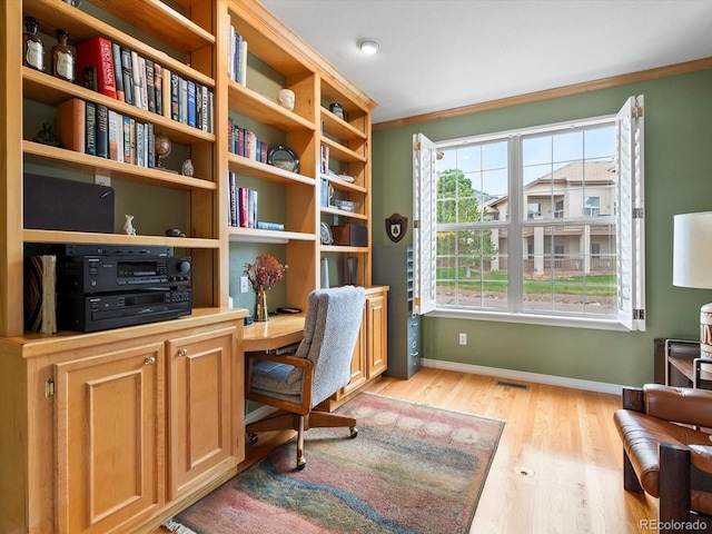 office space featuring built in desk, light wood finished floors, baseboards, visible vents, and ornamental molding