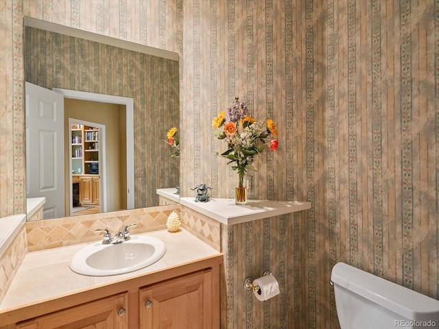 half bathroom with toilet, wallpapered walls, and vanity