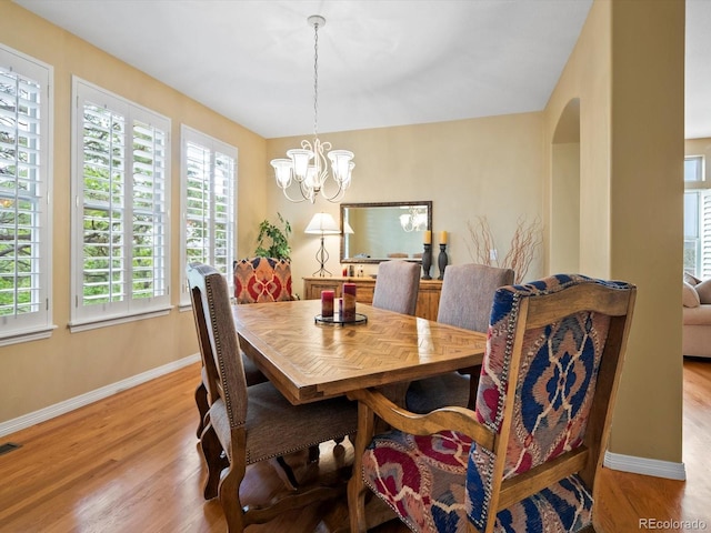 dining room with an inviting chandelier, baseboards, arched walkways, and wood finished floors
