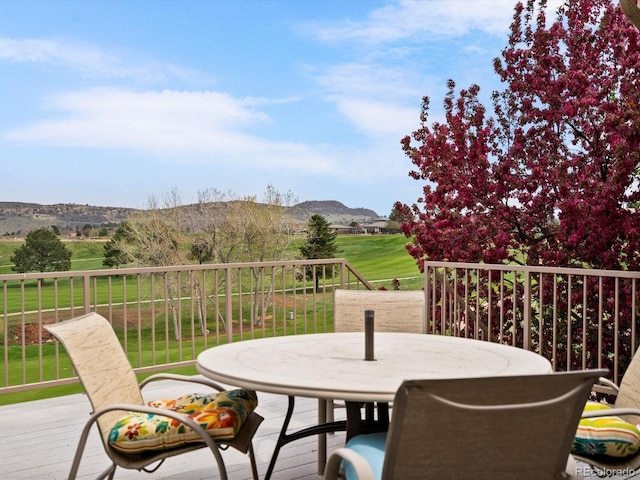 wooden deck featuring a lawn, a mountain view, and outdoor dining space