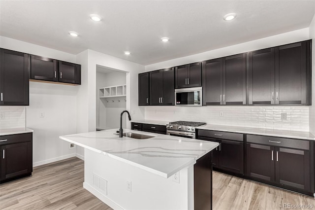 2651 E 102nd Pl, Thornton, CO 80229 - kitchen with appliances with stainless steel finishes, light wood-style floors, tasteful backsplash, an island with sink, and light stone counters