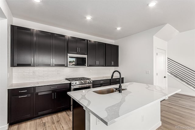 2651 E 102nd Pl, Thornton, CO 80229 - kitchen with stainless steel appliances, light wood-style flooring, dark cabinetry, backsplash, and light stone countertops