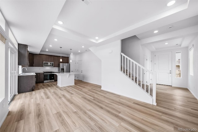 kitchen with light wood-type flooring, light countertops, dark brown cabinets, appliances with stainless steel finishes, and open floor plan