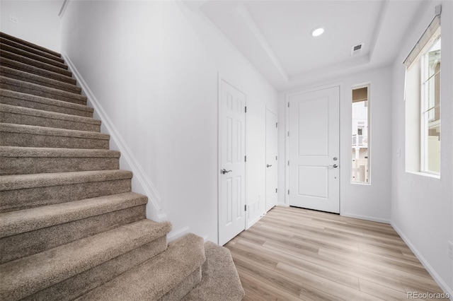 foyer entrance with light wood finished floors, baseboards, stairs, a tray ceiling, and recessed lighting